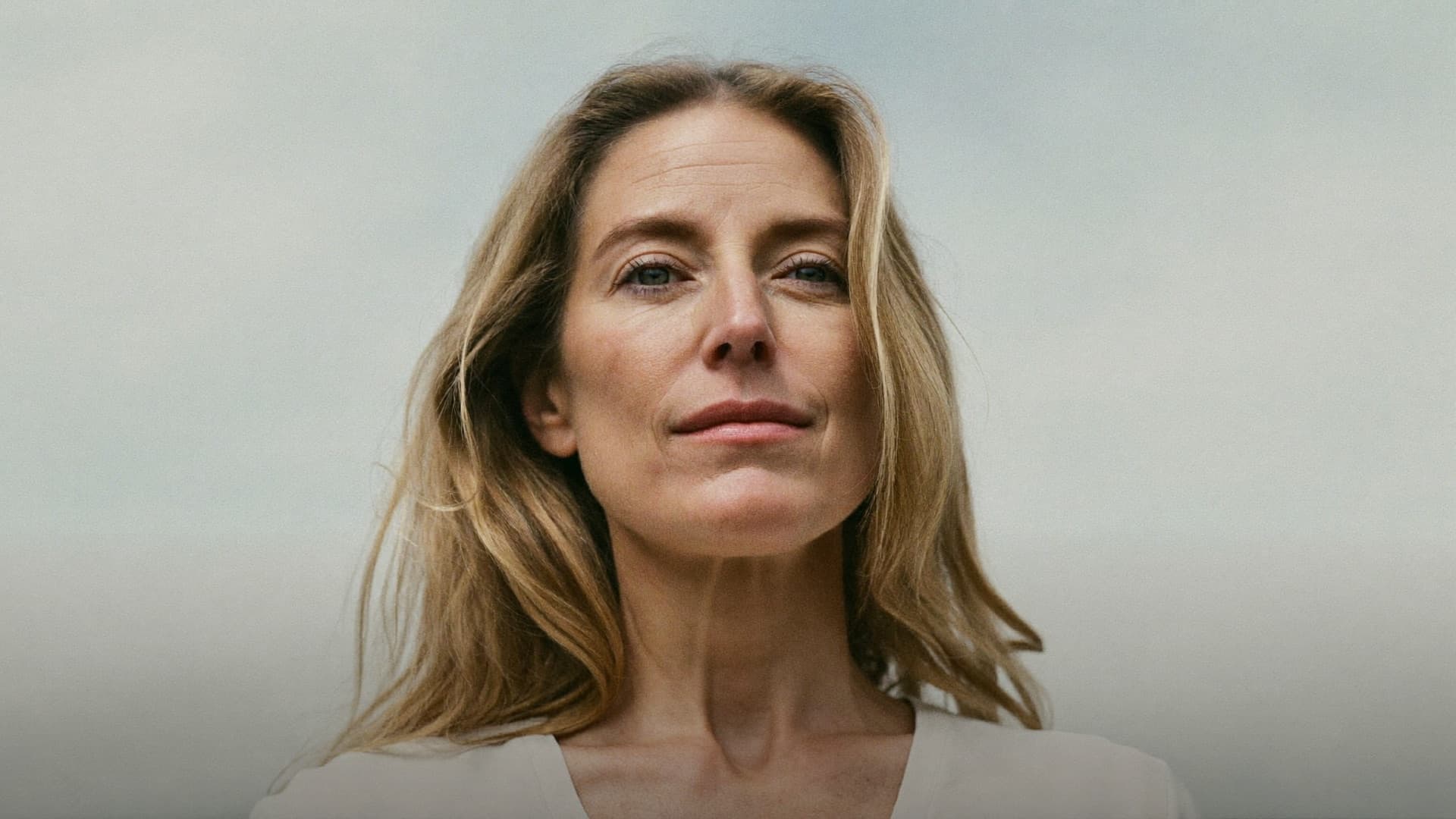 A woman standing outdoors against an overcast sky.